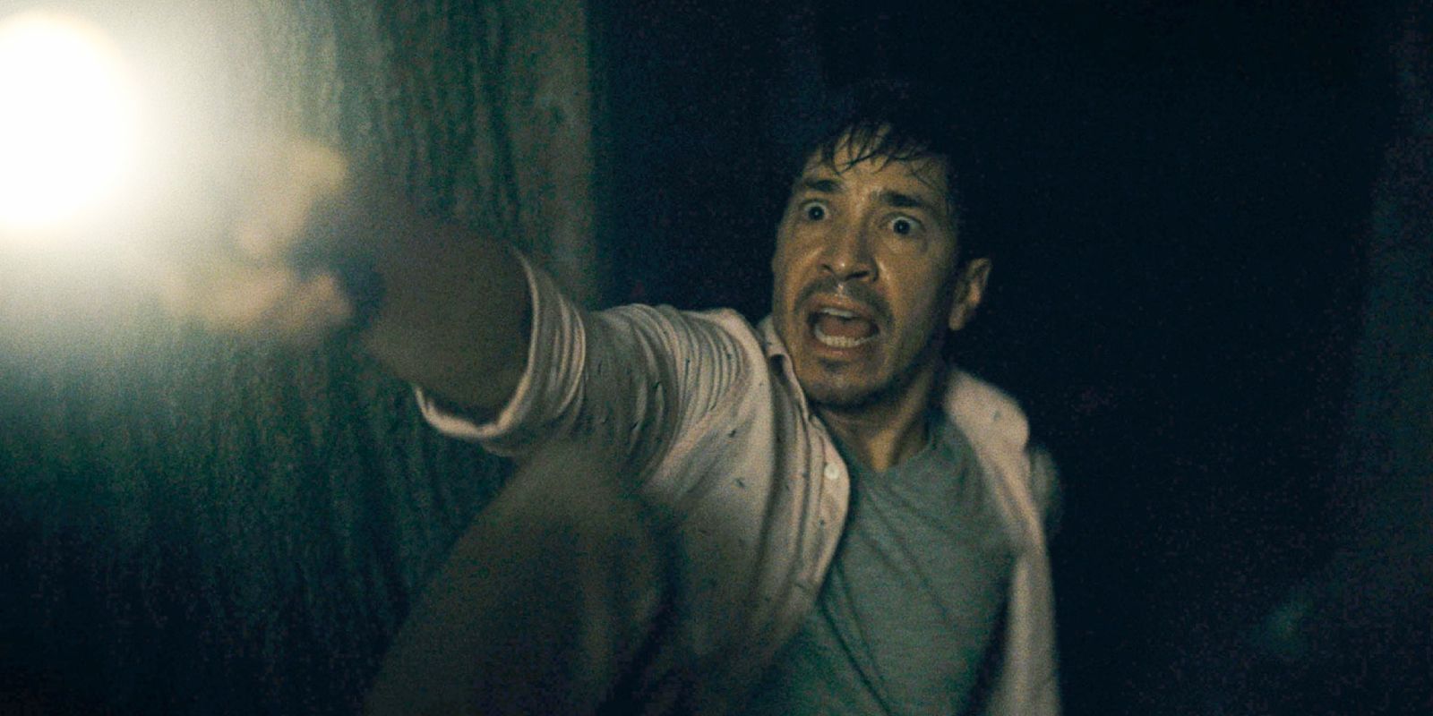 Justin Long pointing a flashlight in the dark and yelling at something off-screen in Barbarian (2022)