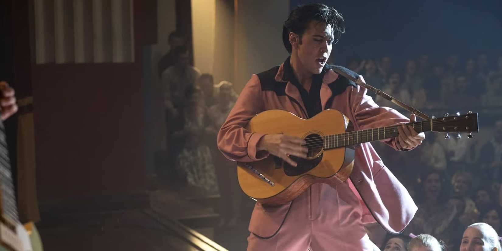 Austin Butler as Elvis Presley, singing on guitar in pink at a live concert, in a still from 'Elvis.'