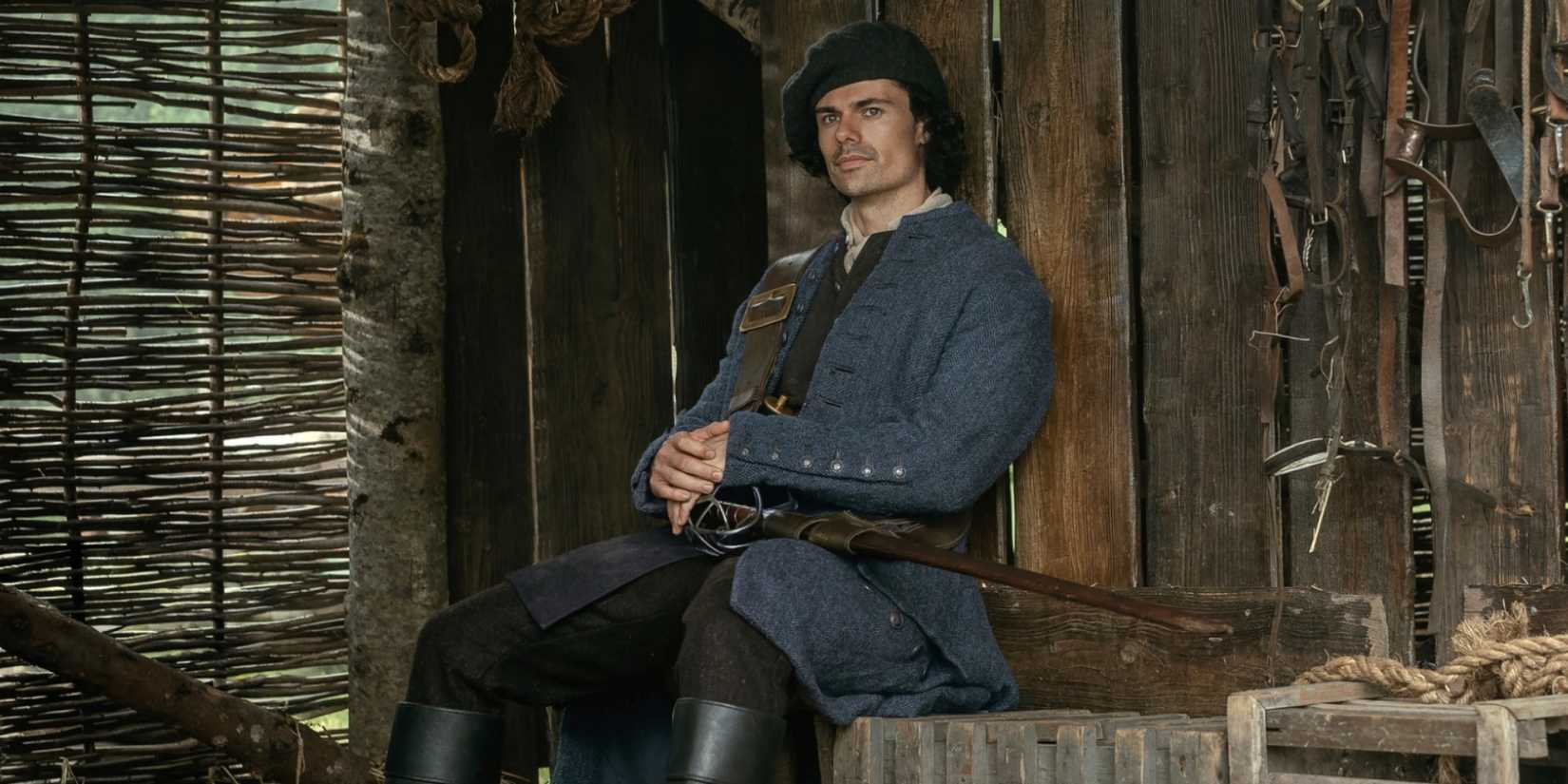 Jamie Roy as Brian Fraser sitting while dressed in a hat, coat and boots in Outlander: Blood of My Blood.