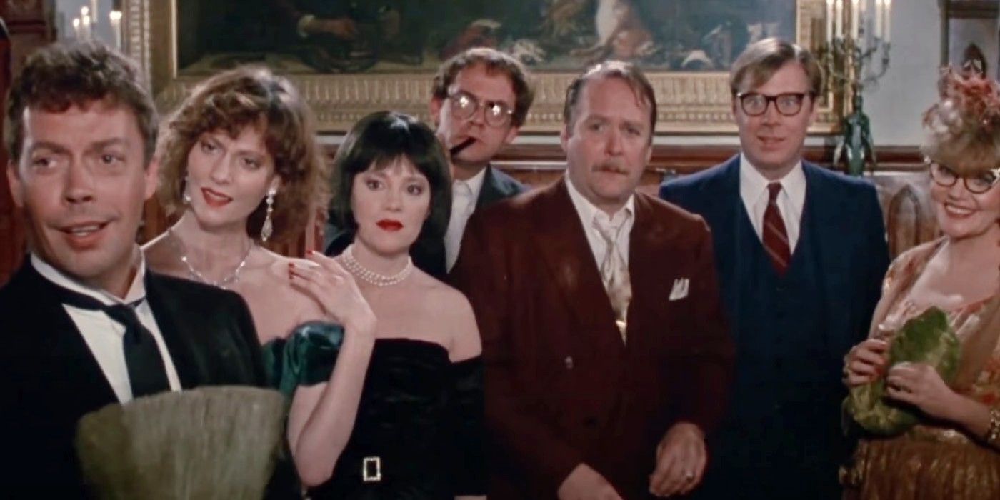 The cast of Clue standing in a row, beginning with Tim Curry clutching the head of a broom on the left.