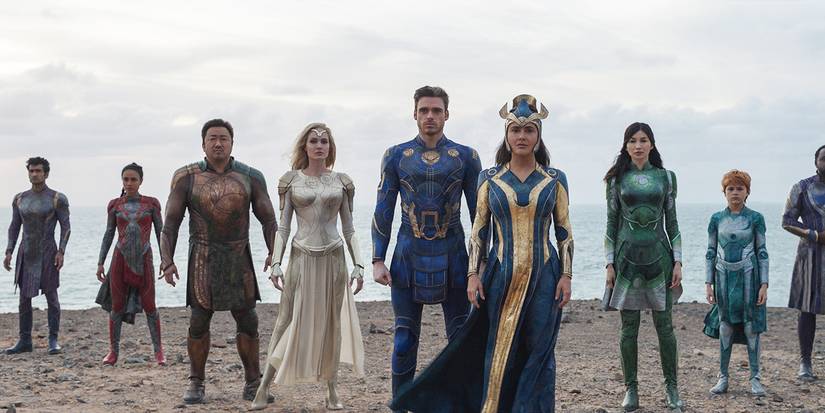 Eternals stand in a line in their hero outfits on the beach