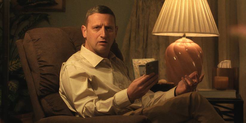 Tim Robinson sitting in a chair with his phone in Friendship