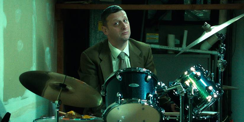 Tim Robinson giving a suspicious look while seated at a drum kit in Friendship