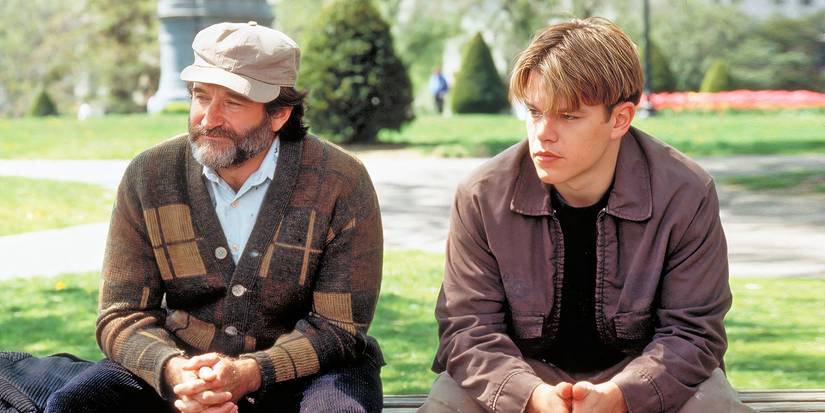 Matt Damon and Robin Williams sitting on a bench outdoors and looking ahead in Good Will Hunting.