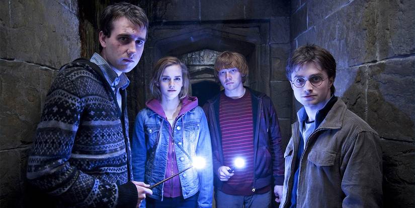 Neville, Hermione, Ron, and Harry with their wands lit looking at the camera