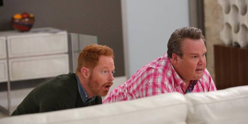 Jesse Tyler Ferguson and Eric Stonestreet hiding behind a sofa in "Phil's Sexy, Sexy House" in 'Modern Family'