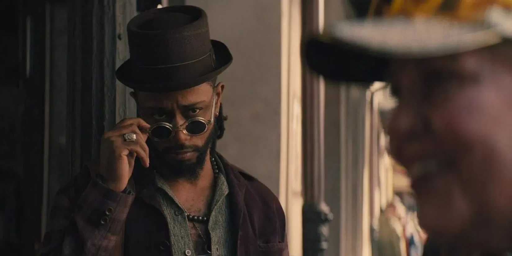 LaKeith Stanfield as Ben Matthias looking over the rim of his glasses at a tourist in Haunted Mansion.