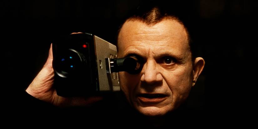 Robert Blake as The Mystery Man holds a video camera up and looks through the lens in Lost Highway.