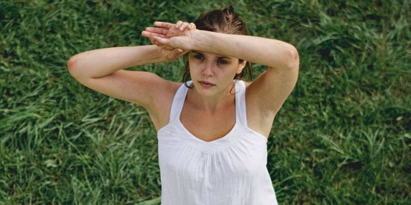 Martha sits in the grass at the cult's commune, shielding her face from the sun in Martha Marcy May Marlene