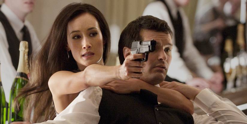 Nikita aiming her gun and using a man as a shield in Nikita