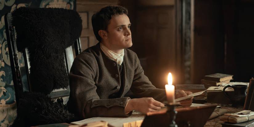 Seamus McLean Ross sitting at a desk and holding a sheet of paper in Outlander: Blood of My Blood Episode 4.
