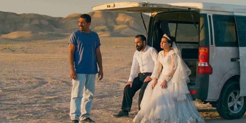 It Was Just an Accident - a bride & groom sit in their open van in the deset; another man stands nearby