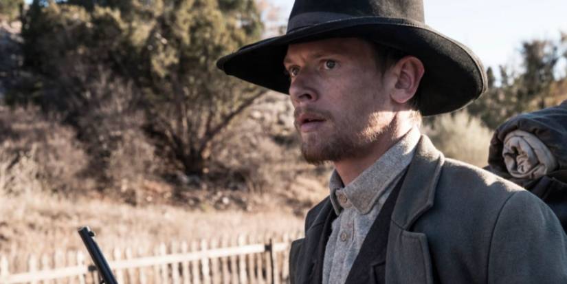 Jack O'Connell as Roy Goode holding a gun and wearing a black hat in 'Godless.'