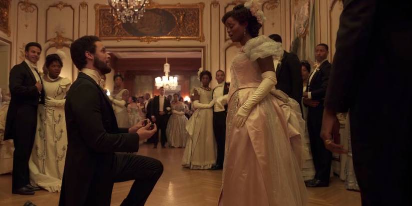 Jordan Donica and Denee Benton as Dr. Kirkland and Peggy Scott wearing a black suit bended one knee and wearing a pink dress in 'The Gilded Age'