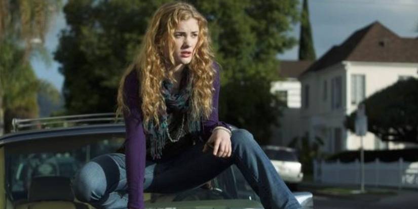 Skyler Samuels as Chloe wearing a purple sweater and crouching on top of a car in 'The Nine Lives of Chloe King.'