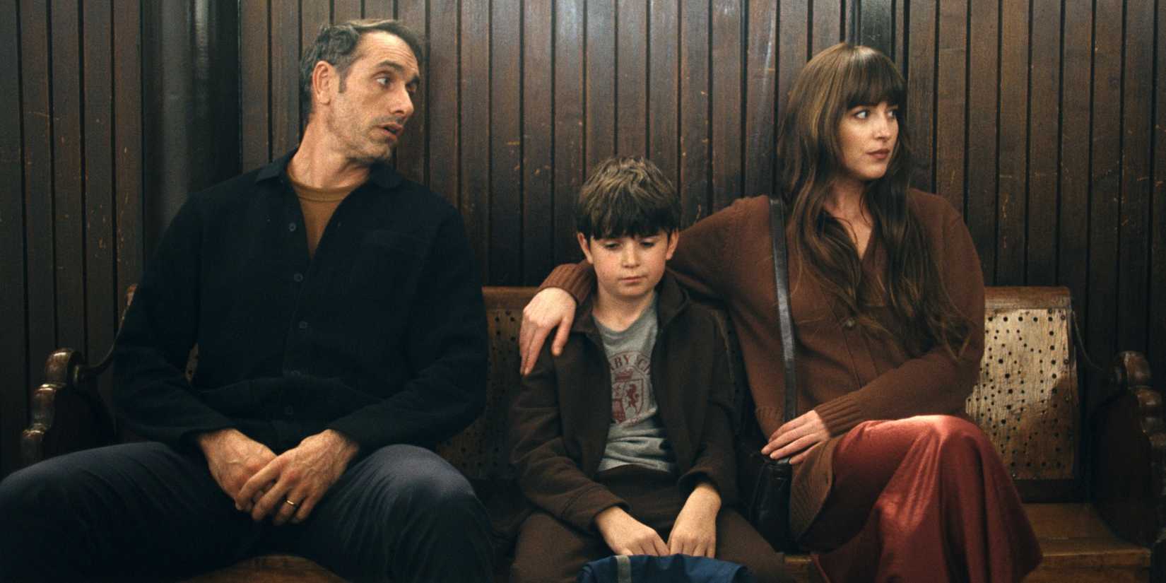 Dakota Johnson as Julie sitting on a bench with Michael Angelo Covino as Paul and their son in Splitsville