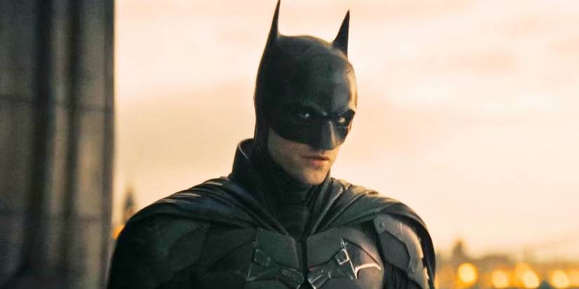 Robert Pattinson as the titular character in The Batman (2022), standing outside at sunrise or sunset while brooding