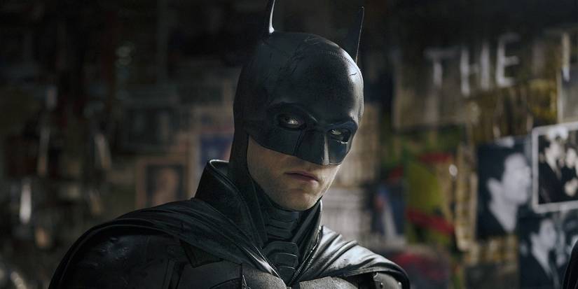Robert Pattinson in the Batman suit looking to the side with a wall of photos behind in The Batman.
