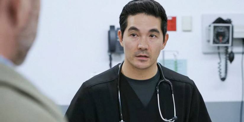 Ken Kirby as Dr. Shen in scrubs wearing a stethoscope talking to someone in 'The Pitt'.