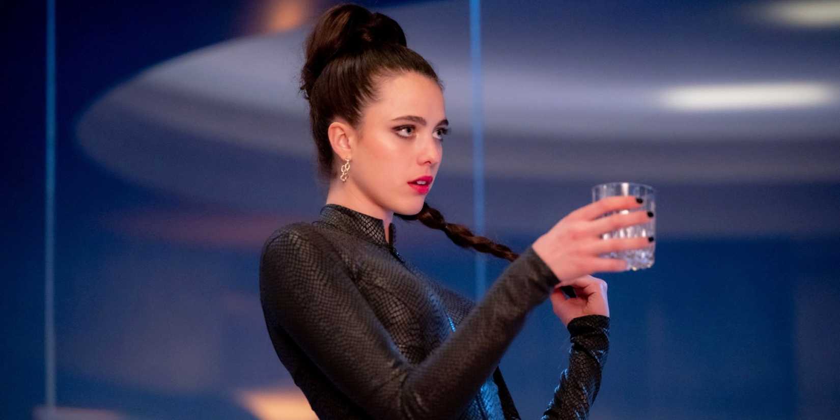 Margaret Qualley sebagai Sue memegang minuman di dalam ruangan yang tampak aneh sambil tampil gaya di The Substance (2024)