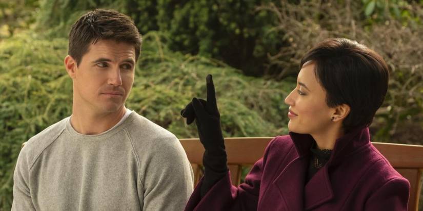 Robbie Amell and Andy Allo talk on a park bench in Upload.