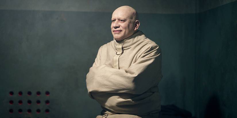 Fred Armisen como el tío Fester sonriendo con una camisa de fuerza en la segunda temporada de Wednesday.