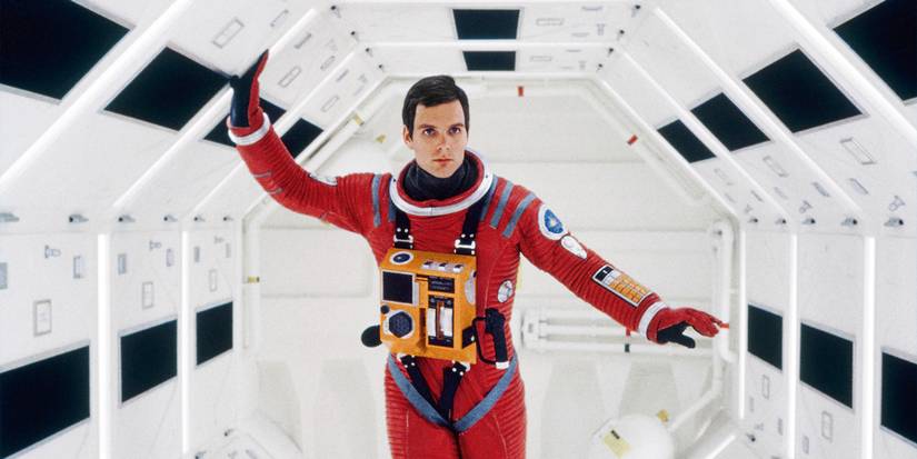 Keir Dullea in a red spacesuit walking through well-lit space pod in 2001: A Space Odyssey.