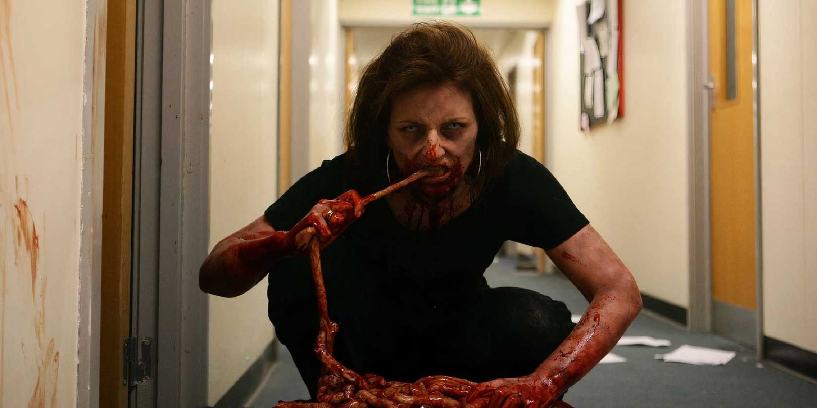 A woman zombie eating guts while looking at the camera in Dead Set