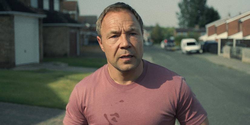 Stephen Graham standing on a street with houses looking worried in Adolescence.