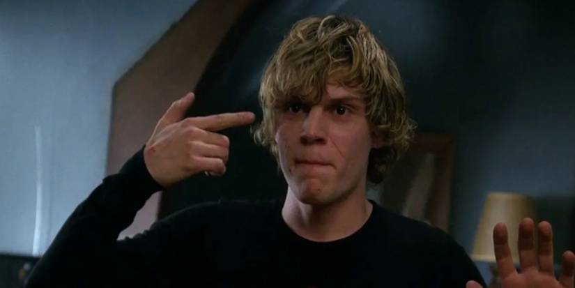 Tate holds a finger to his head while facing the SWAT team in American Horror Story.