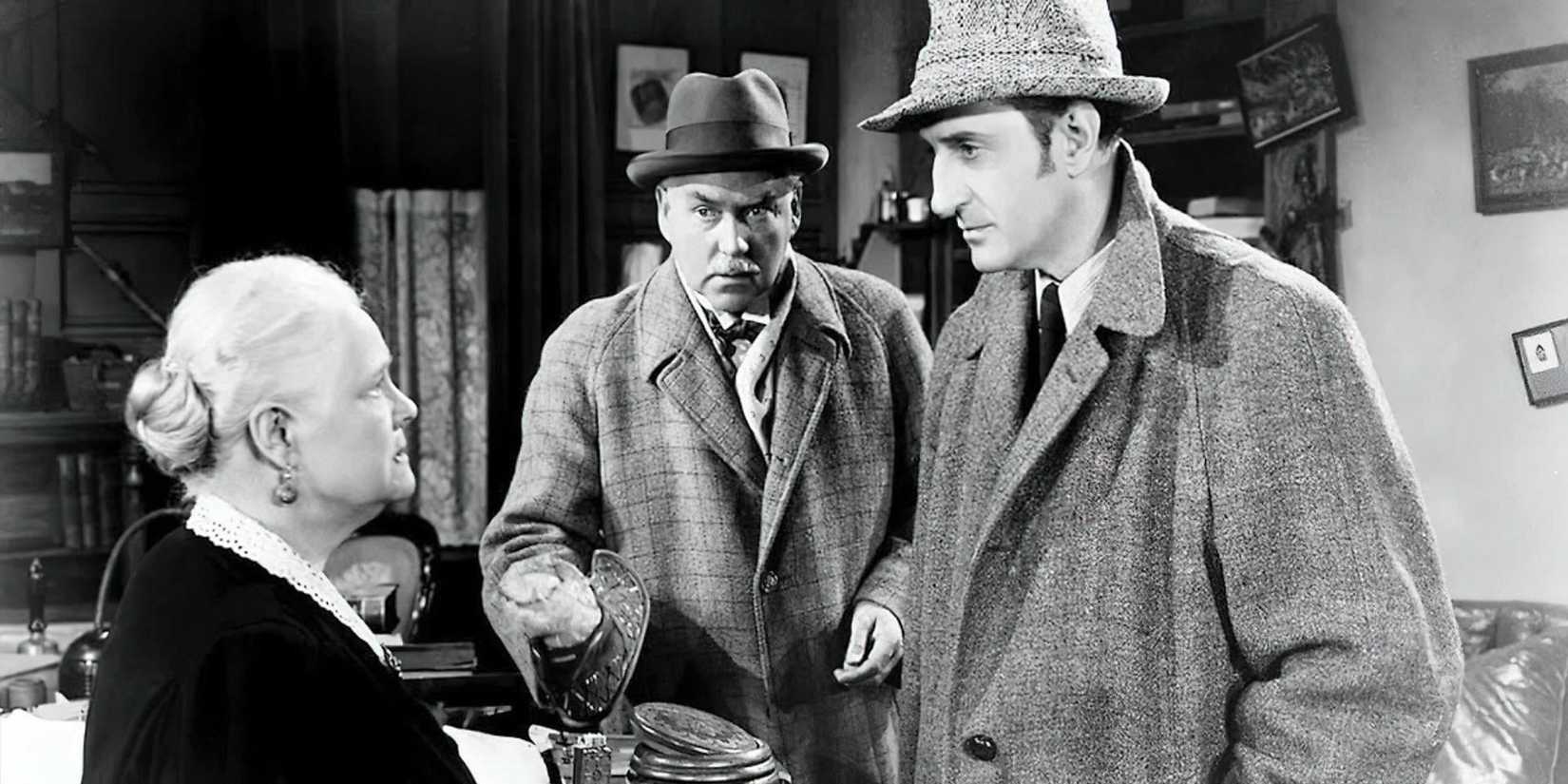 Basil Rathbone as Sherlock Holmes stands in front of a woman as Nigel Bruce as Watson stands next to them in Dressed to Kill (1946).
