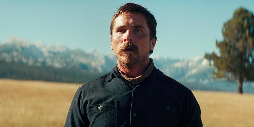 Christian Bale in a uniform standing in an empty field in the Western movie 'Hostiles'