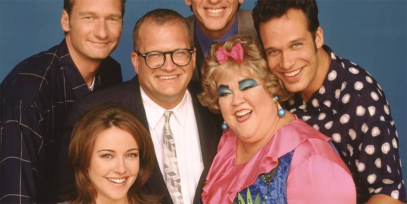 The Drew Carey Show cast posing together and smiling at the camera with a plain background.