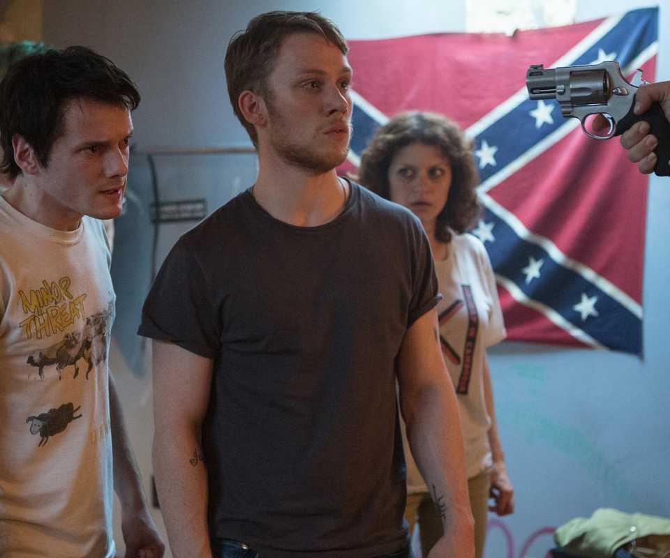 A hand aiming a gun at a group of young people in Green Room