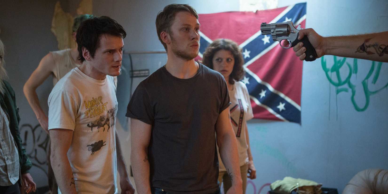 A hand aiming a gun at a group of young people in Green Room