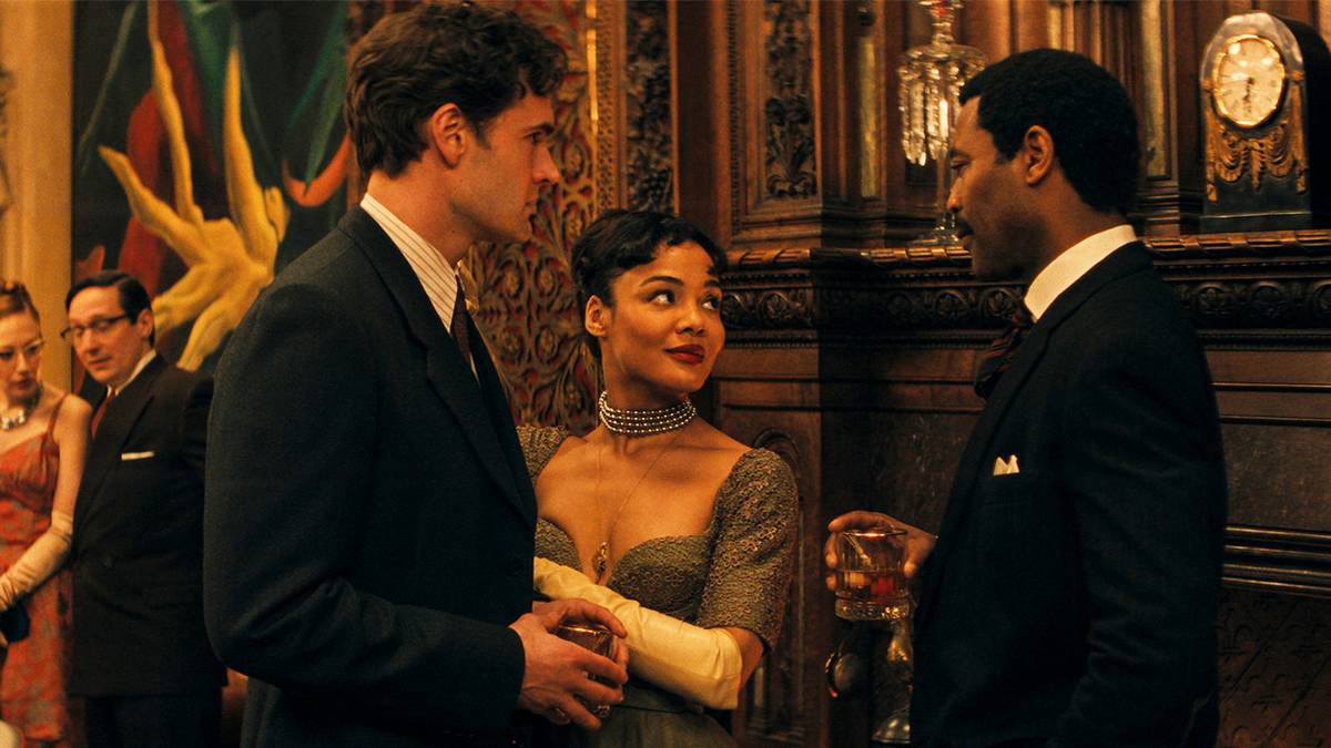 Tessa Thompson, Tom Bateman, and Nicholas Pinnock talk during a fancy party in Hedda