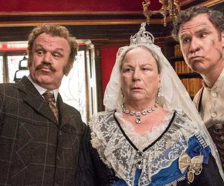Holmes & Watson stand with the Queen looking at something off camera
