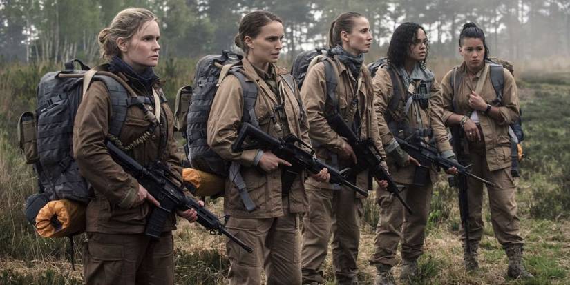 Five armed women, each carrying large backpacks, stand in a line looking at what lies before them.