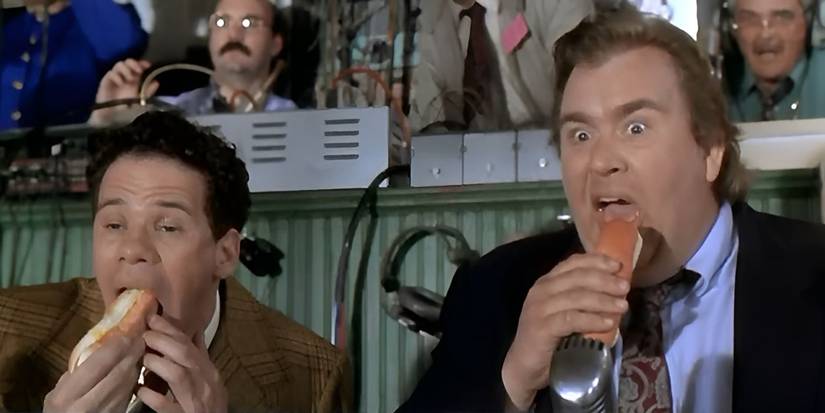 John Candy as a sportscaster about to eat a hot dog looks amazed mid-bite in Rookie of the Year.
