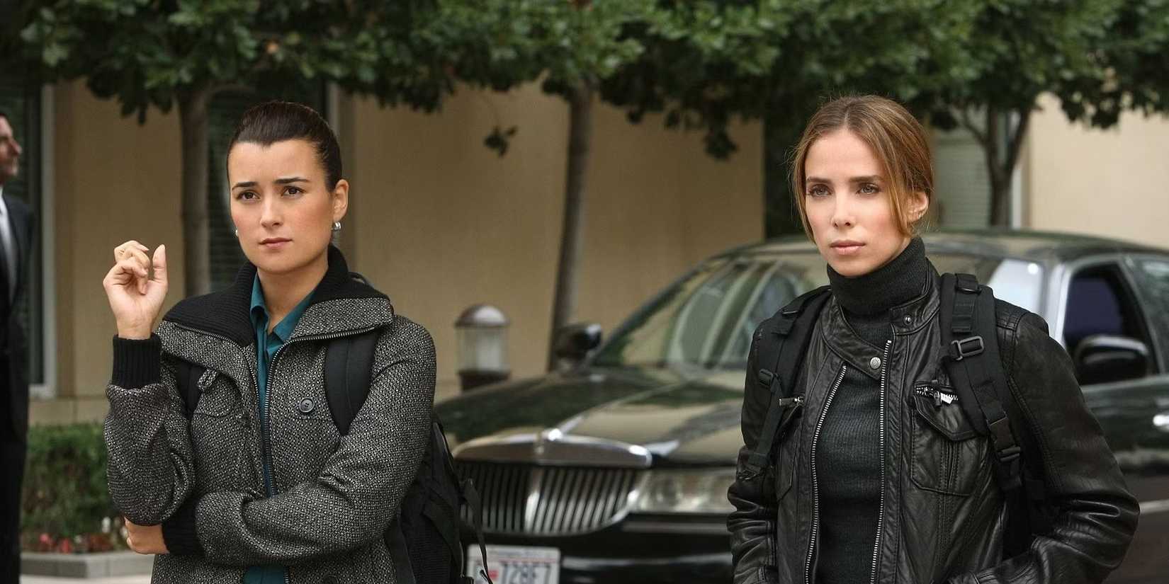 Ziva stands outside with another person and they both look ahead in NCIS. 