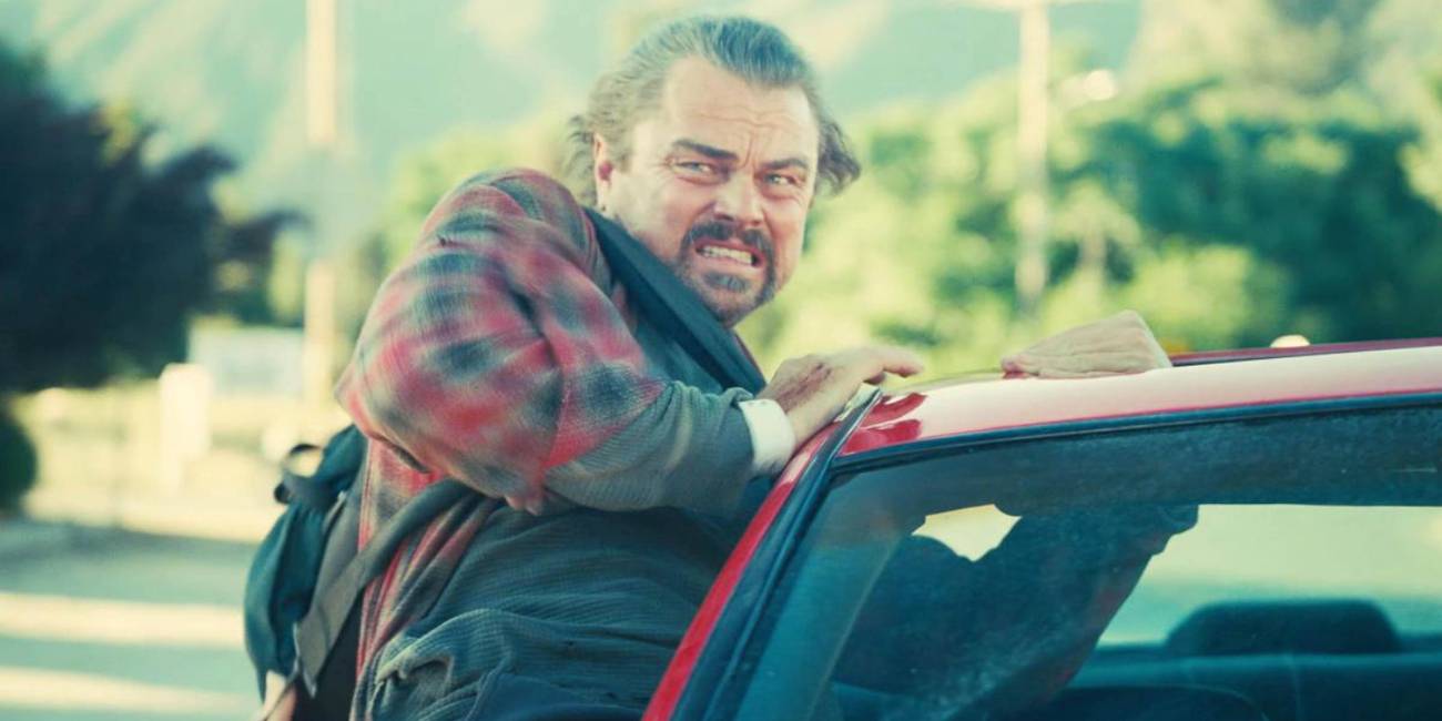 Leonardo DiCaprio leaning out of a moving car with a grimace on his face in One Battle After Another (2025).