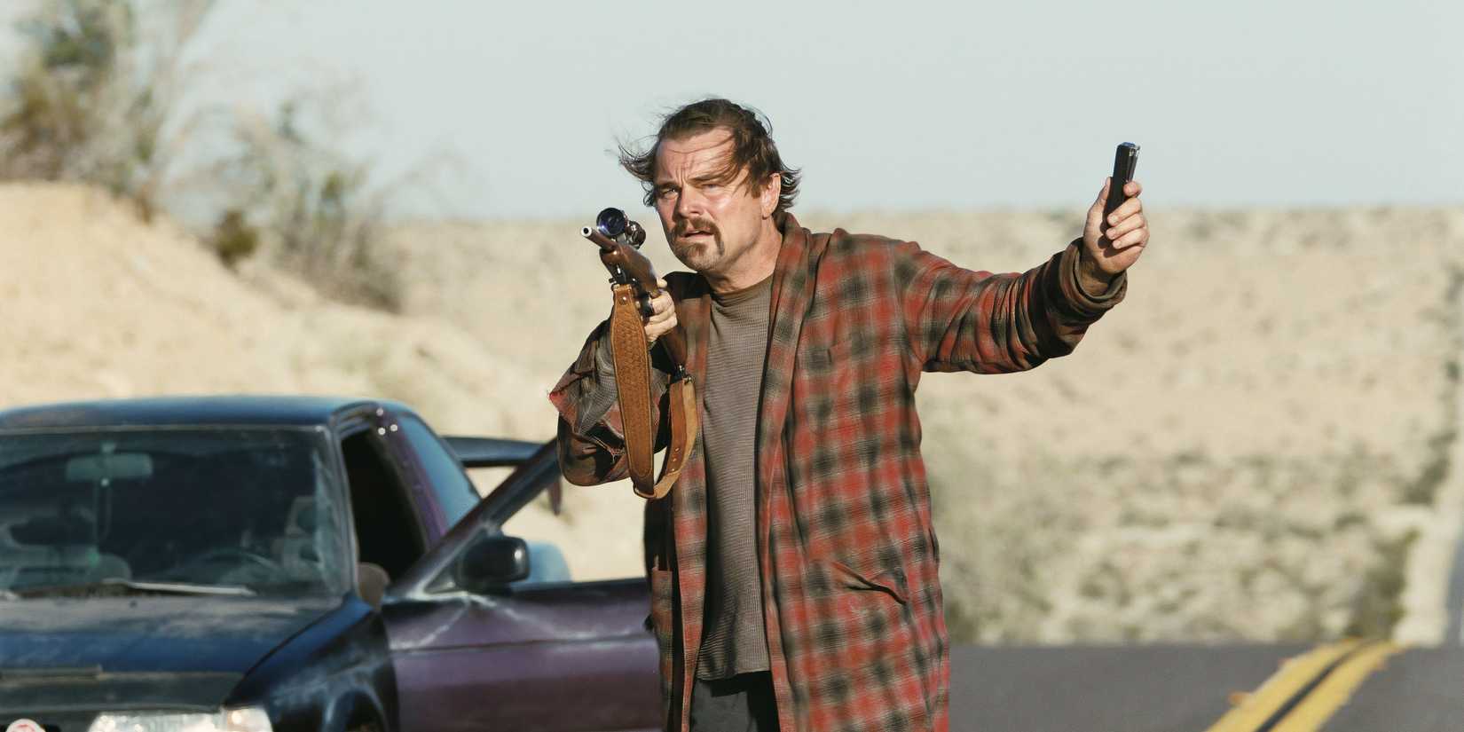 Leonardo DiCaprio in One Battle After Another holding a weapon outside a vehicle