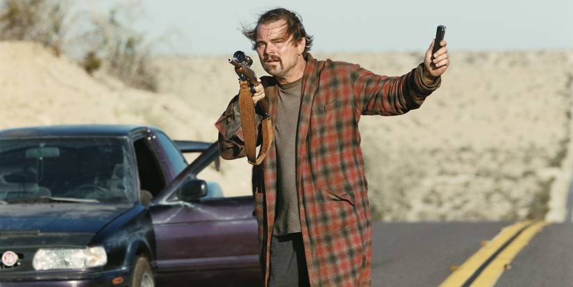 Leonardo DiCaprio holding a weapon in the middle of a highway in One Battle After Another.