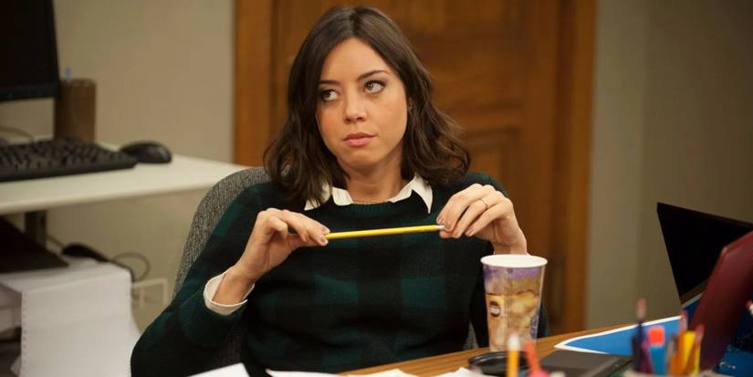 Aubrey Plaza sitting on a desk looking upward in Parks and Recreation