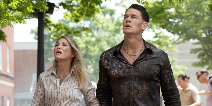 John Cena as Peacemaker in an alternate reality standing with Jennifer Holland as Harcourt in Peacemaker