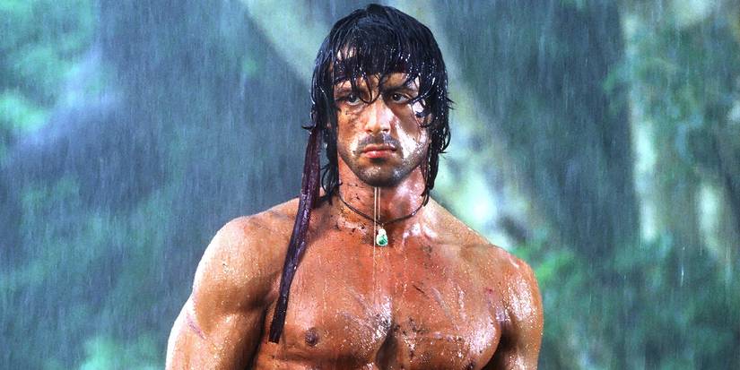 Sylvester Stallone as Rambo standing shirtless in the rain in First Blood Part 2