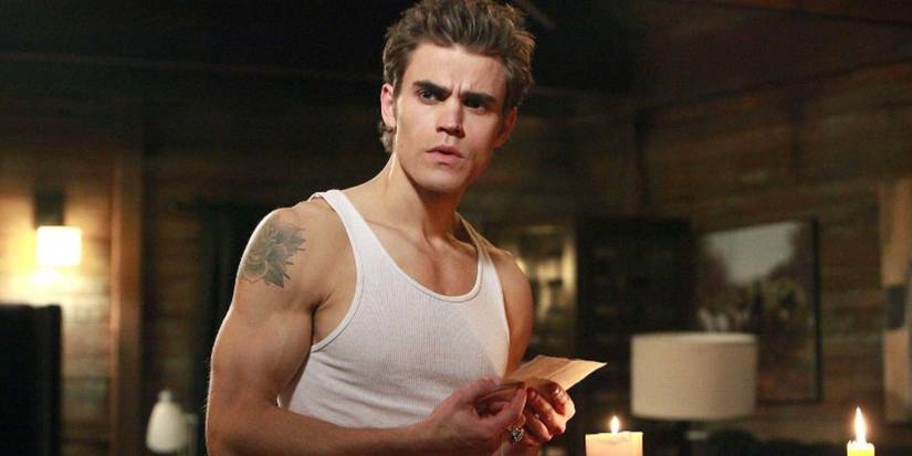 Paul Wesley as Stefan wearing a white tank top standing in a room with candles in 'The Vampire Diaries.'