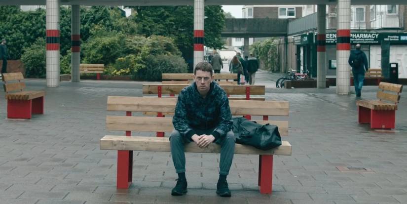 Rob Trew (Edward Davis) sits on a bench in a town square in 'Slow Horses'