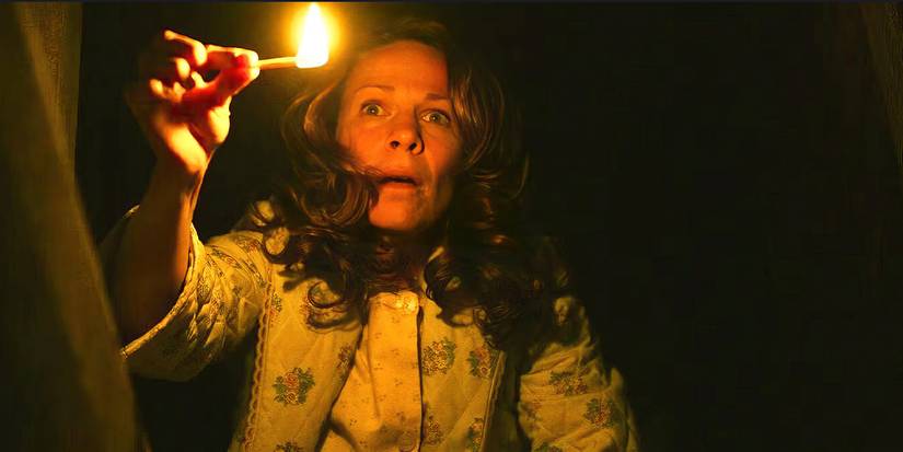 A woman looks scared, holding a single match in a dark place in The Conjuring.