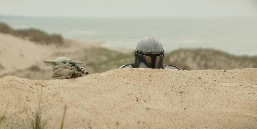 Mando (Pedro Pascal) and Grogu spy from behind a hill in 'The Mandalorian and Grogu'